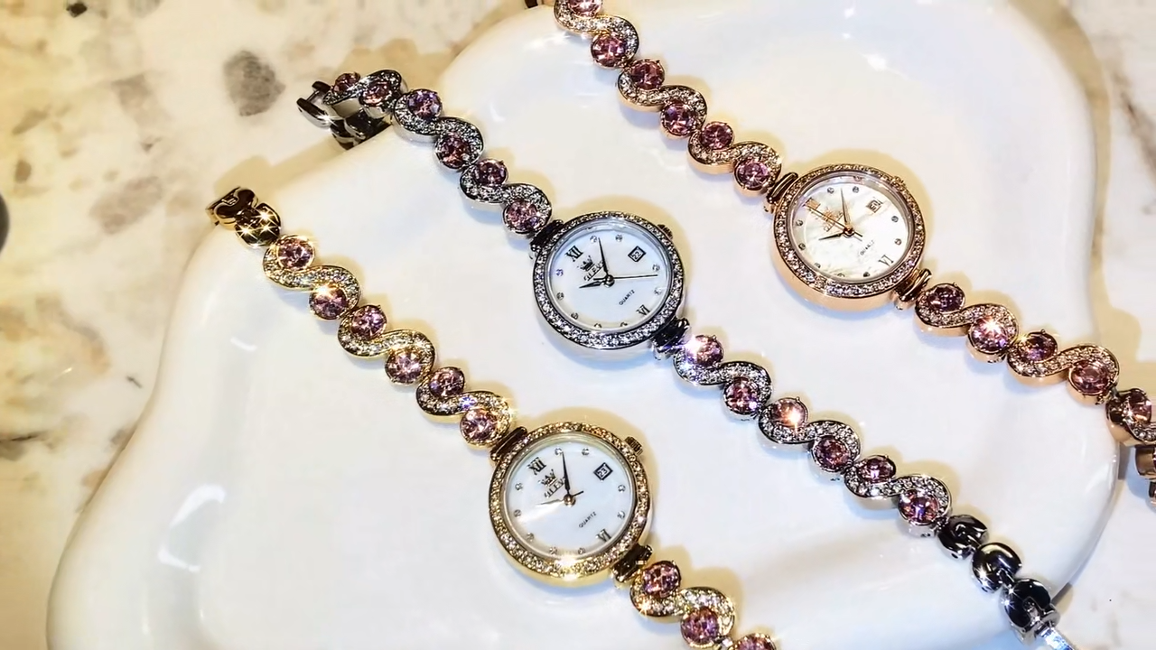 Two gold watches with pink gemstones on a white surface